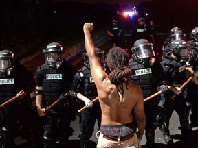 In this photo taken Sept. 20, 2016, protester Braxton Winston stands with his left arm and fist clenched as Charlotte-Mecklenburg police officers form a line on Old Concord Road in Charlotte, N.C., after a police-involved shooting. Winston won an at-large seat on Charlotte's city council during Tuesday's election. (Jeff Siner/The Charlotte Observer via AP)