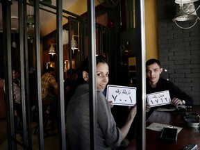 In this Nov. 22, 2017 photo, customer Amr El Gohary, right, and his friend pose for a photograph with plastic plaques that translate to inmates with numbers, as they wait for their food, at prison-themed restaurant 'Food Crime' in the Nile Delta city of Mansoura, 110 kilometers (70 miles) north of Cairo, Egypt. The motif has even drawn policemen like Gohary, impressed by "amazing decor" and amenities like handcuffs and a metal cage that allow him a role reversal. (AP Photo/Nariman El-Mofty)