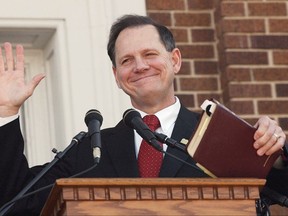 FILE - In this Nov. 6, 2003 file photo, former Alabama Chief Justice Roy Moore holds his Bible as he acknowledges the applause during his speech at the Barrow County Court House in Winder, Ga. Republican Moore's campaign is lashing out again at the news media and accusations of sexual misconduct, but refusing to answer reporters' questions. (AP Photo/Ric Feld, File)