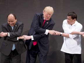 U.S. President Donald Trump, center, reacts as he does the "ASEAN-way handshake" with Vietnamese President Tran Dai Quang, left, and Philippines President Rodrigo Duterte on stage during the opening ceremony at the ASEAN Summit at the Cultural Center of the Philippines, Monday, Nov. 13, 2017, in Manila, Philippines. Trump initially did the handshake incorrectly. Trump is on a five-country trip through Asia traveling to Japan, South Korea, China, Vietnam and the Philippines. (AP Photo/Andrew Harnik)