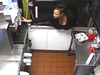 After reaching for a drink, the woman enters through the drive-thru and is seen leaving with a box of items.