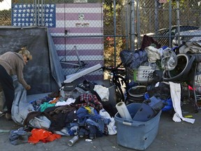 In this Sept. 25, 2017 photo, a woman who was camping in downtown San Diego sorts through her belongings on a sidewalk that was being sprayed with a bleach solution to fight a deadly hepatitis A outbreak. The increased number of hepatitis cases in the homeless population and the geographic spread of the disease led California to declare a state of emergency in October. (AP Photo/Gregory Bull)