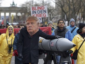 An anti-war protester wears a mask showing US President Donald Trump in Berlin, Germany, Saturday, Nov. 18, 2017 during a demonstration  against nuclear weapons near the Brandenburg Gate. (AP Photo/Michael Sohn)