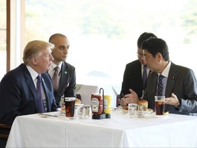 FILE - In this Nov. 5, 2017, file photo from the Prime Minister's Office Facebook page, U.S. President Donald Trump, left, listens to Japanese Prime Minister Shinzo Abe, right, during a lunch of hamburgers from Munch's Burger Shack at Kasumigaseki Country Club in Kawagoe, Japan. The cheeseburger Trump had is still drawing lines to the Tokyo burger joint. (Cabinet Public Relations Office of Japan via AP)