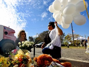 Michelle Trigo, right, carries balloons to lay near the site of Sunday's shooting at the First Baptist Church of Sutherland Springs, Texas, Monday, Nov. 6, 2017.  Trigo's friend Malinda Lamford, left, brought roses to lay at the small memorial growing down the street along Highway 87. (Mark Mulligan/Houston Chronicle via AP)