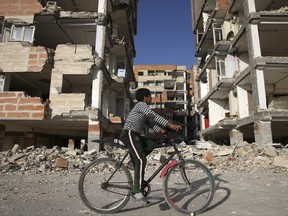 An earthquake survivor rides his bicycle in front of damaged buildings, in a compound which was built under the Mehr state-owned program, in Sarpol-e-Zahab in western Iran, Wednesday, Nov. 15, 2017. Survivors in Iran are awaiting badly needed aid, three days after a powerful earthquake along the Iraq border killed hundreds and left thousands injured. (AP Photo/Vahid Salemi)