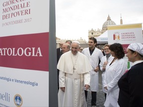 Pope Francis meets with volunteers during a surprise visit to a small facility near St. Peter's Square where doctors on a volunteer basis give poor people medical exams, at the Vatican, Thursday, Nov. 17, 2017. Francis on Thursday decried that, increasingly, only the privileged can afford sophisticated medical treatments and urged lawmakers to ensure that health care laws protect the "common good." Writing on stand at left reads "Dermatology."v(L'Osservatore Romano/Pool Photo via AP)