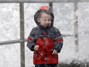 Archer Christiansen, 3, braces himself against wind and a breaking wave as he walks with his parents in a windstorm along the Puget Sound Monday, Nov. 13, 2017, in Seattle. Thousands of people lost power in western Washington state after high winds swept through overnight, and the National Weather Service says more strong winds are expected. The weather service said Monday that many areas will continue to see gusts topping 50 mph, with even stronger winds on the coast and in north-central and northeastern Washington. (AP Photo/Elaine Thompson)