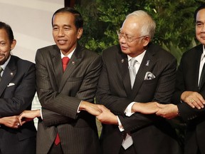 From left, Brunei Sultan Hassanal Bolkiah, Indonesia President Joko Widodo, Malaysia Prime Minister Najib Razak and Thailand Prime Minister Prayut Chan-ocha link arms as they pose for a group photo during the East Asia Summit in Manila, Philippines on Tuesday Nov. 14, 2017. (Erik De Castro/Pool Photo via AP)