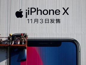 In this Monday, Oct. 30, 2017 photo, workers on a suspended platform replace an advertisement poster for the new iPhone X on a building in Beijing. Chinese manufacturing activity expanded in October at a slower pace than in the previous month as output weakened on softer demand in the world's No. 2 economy, according to an official survey released Tuesday. (AP Photo/Andy Wong)