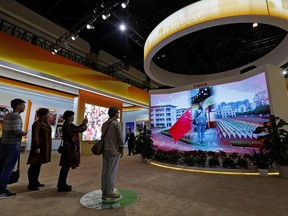 FILE - In this Monday, Oct. 23, 2017, file photo, visitors watch a man appearing on a screen as he experiences a national anthem flag raising ceremony at an exhibition highlighting China's achievements at the Beijing Exhibition Hall in the capital city where the 19th Party Congress is held in Beijing. On Saturday, Nov. 4, 2017, China's rubber-stamp legislature has made disrespecting the national anthem a criminal offense punishable by up to three years in prison. (AP Photo/Andy Wong, File)
