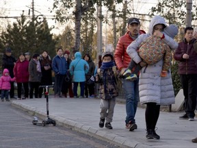 FILE - In this Friday, Nov. 24, 2017, file photo, a woman carries a child as they arrive at the RYB kindergarten in Beijing, China,. Authorities in China say they have detained a woman suspected of abusing children at a Beijing kindergarten run by a U.S.-listed company in a case that has caused nationwide anger. (AP Photo/Ng Han Guan)