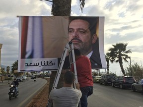 Workers hang a poster of outgoing Prime Minister Saad Hariri with Arabic words that read, "We are all Saad," on a seaside street in Beirut, Lebanon, Thursday, Nov. 9, 2017. Hezbollah has called on Saudi Arabia to stay out of Lebanese affairs, saying the resignation of Prime Minister Saad Hariri, announced from Riyadh over the weekend, "has raised many questions." (AP Photo/Hussein Malla)