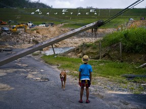 FILE - In this Oct. 17, 2017 file photo, a boy accompanied by his dog watches the repairs of Guajataca Dam, which cracked during the passage of Hurricane Maria, in Quebradillas, Puerto Rico. Experts said on Thursday, Nov. 16, 2017, that Puerto Rico could face nearly two decades of further economic stagnation and a steep drop in population as a result of Maria. (AP Photo/Ramon Espinosa, File)
