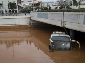 People are reflected in the front window of a flooded bus as water engulfs an interchange of a highway in Elefsina, western Athens, on Wednesday, Nov. 15, 2017. Flash floods in the Greek capital's western outskirts Wednesday converted roads into raging torrents of mud and debris, killing at least five people and inundating homes and businesses. (AP Photo/Petros Giannakouris)