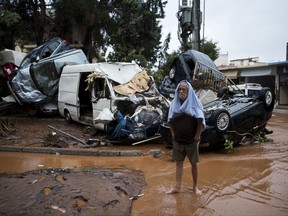 A barefoot man stands in front of a pile of vehicles in the municipality of Madra western Athens, on Wednesday, Nov. 15, 2017. Flash floods in the Greek capital's western outskirts Wednesday turned roads into raging torrents of mud and debris, killing at least nine people, inundating homes and businesses and knocking out a section of a highway. (AP Photo/Petros Giannakouris)
