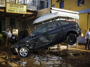 Staff at a car rental store clean up damage in front of a washed up vehicle following a powerful storm on the Greek island of Symi, on Tuesday, Nov. 14, 2017. Authorities declared a state of emergency on the east Aegean Sea island after the storm caused extensive flooding, road damage, and power outages. (Argiris Madikos /Eurokinissi via AP)