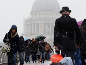 A gentleman wearing a bowler is among pedestrians crossing the Millennium Bridge (with St Paul's Cathedral in the background) as snow falls over central London on December 10, 2017.