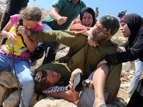 This file photo taken on August 28, 2015 shows Palestinian Ahed Tamimi (L) fighting with other members of her family to free a Palestinian boy (bottom) held by an Israeli soldier (C) during clashes between Israeli security forces and Palestinian protesters in the West Bank village of Nabi Saleh near Ramallah. Israel's army arrested Ahed Tamimi on December 19, 2017, after a video went viral of her slapping Israeli soldiers in the occupied West Bank as they remained impassive.