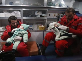 Syrian paramedics distract children inside an ambulance on the second night of an evacuation operation led by the Syrian Red Crescent and the International Committee of the Red Cross in Douma in the eastern Ghouta region on the outskirts of the capital Damascus late on December 27, 2017.