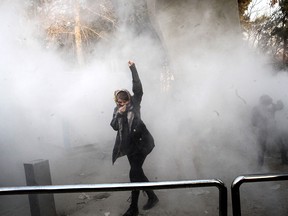 An Iranian woman raises her fist amid the smoke of tear gas at the University of Tehran during a protest driven by anger over economic problems, in the capital Tehran on December 30, 2017.
