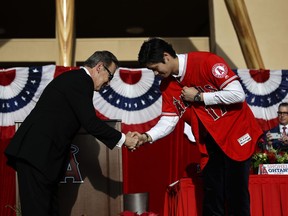Baseball player Shohei Ohtani, right, of Japan, shakes hands with Los Angeles Angels owner Arte Moreno as he puts on his jersey during a news conference at Angel Stadium, Saturday, Dec. 9, 2017, in Anaheim, Calif. Ohtani is bringing his arm and bat to the Angels, pairing him with two-time MVP Mike Trout.