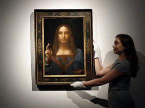FILE- In this Oct. 24, 2017 file photo, an employee poses with Leonardo da Vinci's "Salvator Mundi" on display at Christie's auction rooms in London. An official in the United Arab Emirates says the new Louvre museum in Abu Dhabi is "very proud" to have acquired a painting by Leonardo da Vinci that sold for a staggering $450 million last month.