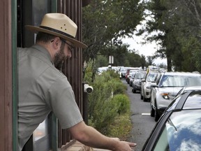 FILE - In this Aug. 2, 2015, file photo, Nate Powell, an employee with Grand Canyon National Park, collects an entrance fee an entrance gate at Grand Canyon National Park, Ariz. National parks in the U.S. will sharply drop the number of days it allows visitors to get in for free. After waiving entrance fees for 16 days in 2016 and 10 days in 2017, the National Park Service announced Tuesday, Dec. 12, 2017, that it will have just four no-cost days in 2018.