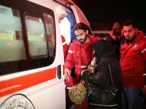 In this photo released by the Syrian official news agency SANA, members of the Syrian Arab Red Crescent help a woman who carries a baby to get inside an ambulance during a human evacuation of sick people from the eastern Ghouta, near Damascus, Syria, Wednesday, Dec. 27, 2017.