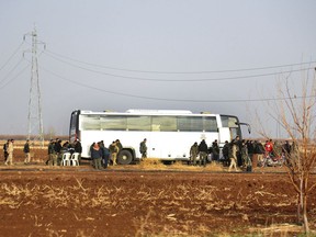 In this photo released on Friday, Dec. 29, 2017 by the Syrian official news agency SANA, Syrian government forces stand next to a bus which is waiting to evacuate Syrian militants and their families from Beit Jin village, in the southern province of Daraa, Syria. Dozens of Syrian militants and their families have left aboard buses an area where they have been besieged by government forces near the Israeli-occupied Golan Heights part of a deal to clear yet another district from insurgents. (SANA via AP)