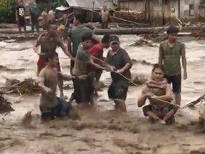 In this photo made from video by Aclimah Disumala, Friday, Dec. 22, 2017, villagers cross raging flood waters in Lanao del Norte, Zamboanga Pennisula, southern Philippines.
