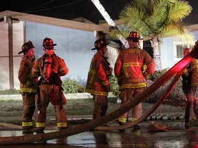 Firefighters stand in front of the house where a small plane crashed into it in San Diego, Saturday, Dec. 9, 2017. Authorities in southern California say at least two people are dead after a single-engine, six-seat Beech BE36 Bonanza crashed into a home. The plane had taken off from Montgomery Field about a half mile away.
