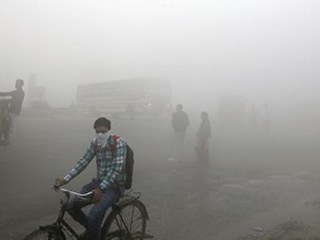 FILE - In this Nov. 10, 2017 file photo, Indian commuters wait for transport amid a thick blanket of smog on the outskirts of New Delhi, India. The petroleum coke being burned in countless factories and plants is contributing to dangerously filthy air in India, which already has many of the world's most polluted cities. India's energy-hungry industries like petcoke because it's cheaper and burns hotter than coal; they also defend their use by saying they're recycling a waste that's being produced anyway. (AP Photo/Altaf Qadri, File)