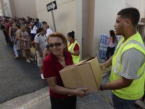 In this Dec. 21, 2017 photo, Doris Martínez receives supplies and water from municipal staff outside the City Hall in Morovis, Puerto Rico. Over 30,000 residents of that mountain town wait for the restoration of electric power service, one of the last municipalities of Puerto Rico that remains completely in the dark more than three months after the passage of Hurricane Maria.