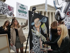 As Janae Stracke, left, and Annabelle Rutledge, both with Concerned Women for America, hold up signs, as Jessica Haas, of Indianapolis, paints during a rally with supporters of cake artist Jack Phillips outside of the Supreme Court which is hearing the 'Masterpiece Cakeshop v. Colorado Civil Rights Commission' today, Tuesday, Dec. 5, 2017, in Washington.