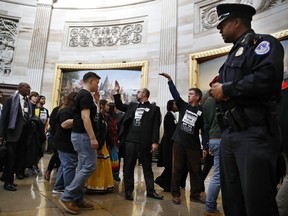 With shirts saying "fight poverty not the poor," people with the "Poor People's Campaign" gesture the group to remain quiet as the group leaves the Capitol Rotunda after praying in an act of civil disobedience in protest of the GOP tax overhaul, Monday, Dec. 4, 2017, on Capitol Hill in Washington.