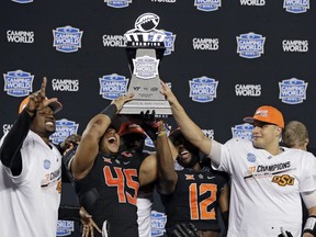 Oklahoma State players, from left, Tre Flowers, Chad Whitener (45), Kirk Tucker (12) and quarterback Mason Rudolph hold up the trophy after Oklahoma State defeated Virginia Tech 30-21 in the Camping World Bowl NCAA college football game Thursday, Dec. 28, 2017, in Orlando, Fla.