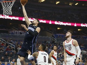 Portland Trail Blazers center Jusuf Nurkic (27) and guard Damian Lillard (0) watch as Orlando Magic center Nikola Vucevic, top left, lays in a basket during the first quarter of an NBA basketball game in Orlando, Fla., Friday, Dec. 15, 2017.