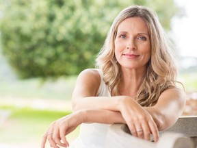 Happy senior woman relaxing on bench in the lawn. Close up face of a mature blonde woman smiling and looking at camera. Retired woman in casuals sitting outdoor in a summer day.