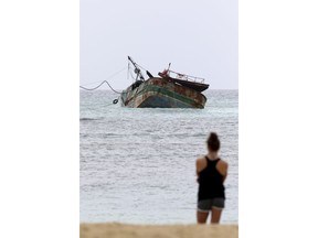 In this Saturday, Dec. 2, 2017 photo, a woman watches as a salvage crew works to refloat the 79-foot Pacific Paradise so it can be removed from a reef off the beaches of Waikiki, in Honolulu. After being filled with foam and water to regain buoyancy, the fishing vessel was connected to a tugboat and hauled off the reef Wednesday, Dec. 6.