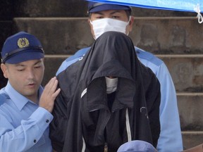 In this May 20, 2016, file photo, police officers escort Kenneth Shinzato, center, out of Uruma Police Station in Uruma on the southern Japanese island of Okinawa.