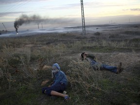 Palestinian protesters cover from teargas fired by Israeli troops during clashes on the Israeli border with Gaza, Monday, Dec. 11, 2017.