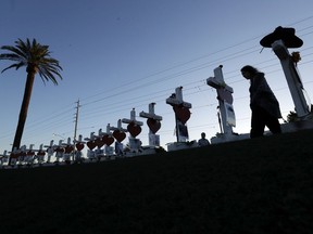 FILE - In this Oct. 6, 2017, file photo, Manuela Barela passes crosses set up to honor those killed during the mass shooting in Las Vegas. A coroner in Las Vegas says all 58 victims in the Oct. 1 mass shooting on the Las Vegas Strip died of gunshot wounds. Clark County Coroner John Fudenberg told The Associated Press on Thursday, Dec. 21, that all the cases were ruled homicides.