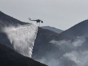 In this photo provided by the Santa Barbara County Fire Department, a Sikorsky S-64 Skycrane makes a water drop on hot spots along the hillside east of Gibraltar Road in Santa Barbara, Calif., Sunday morning, Dec. 17, 2017. One of the largest wildfires in California history is now 40 percent contained but flames still threaten coastal communities as dry, gusty winds are predicted to continue.