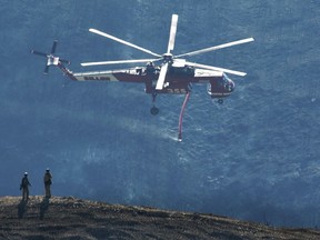 In this photo provided by the Santa Barbara County Fire Department, a Skycrane helicopter passes firefighters atop a hillside while coming in for a water drop below E. Camino Cielo in Santa Barbara, Calif., Tuesday, Dec. 19, 2017. Although some evacuations were lifted Monday and more residents were being allowed to return Tuesday, hillside homes are still threatened in Santa Barbara, where firefighters mounted an aggressive air attack on stubborn flames. Officials estimate that the Thomas Fire will grow to become the biggest in California history before full containment, expected by Jan. 7, 2018.