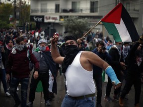 A protester throws a stone as others hold Palestinian flags during a demonstration in front of the U.S. embassy in Aukar, east of Beirut, Lebanon.