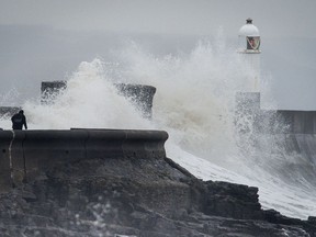 A man watches waves break on the harbour wall at Porthcawl, South Wales, as heavy snowfall across parts of the UK, Sunday Dec. 10, 2017.  Severe weather is forecast across much of eastern Europe as storm conditions approach from the Atlantic.
