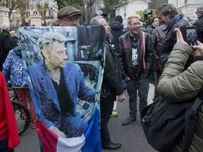 French fan Andre Duval holds a portrait of Johnny Hallyday outside his house in Marnes-la-Coquette, outside Paris, Wednesday, Dec.6, 2017. Johnny Hallyday, France's biggest rock star for more than half a century and an icon who packed sports stadiums and all but lit up the Eiffel Tower with his pumping pelvis and high-voltage tunes, has died. He was 74.