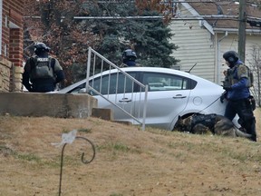 Law enforcement officers look at a house in Bellefontaine Neighbors, Mo., on Thursday, Dec. 14, 2017, during a standoff between a suspect and the police.  A gunman shot two suburban St. Louis police officers in the torso before barricading himself inside a home,  but bulletproof vests saved both officers from serious injury.