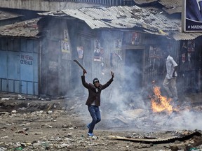 FILE - In this Saturday, Aug. 12, 2017 file photo, a man brandishing a "panga" machete challenges police near a burning barricade during clashes between police and protesters in the Mathare slum of Nairobi, Kenya. A human rights watchdog said Wednesday, Dec. 20, 2017 that 92 people were killed during Kenya's months of election turmoil and dozens of others were sexually assaulted.